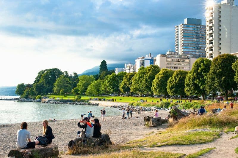 A photo of english bay with lush greenery and high rises, along with people sitting on the beach