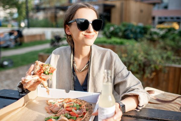 A woman in sunglasses eating pizza in a park
