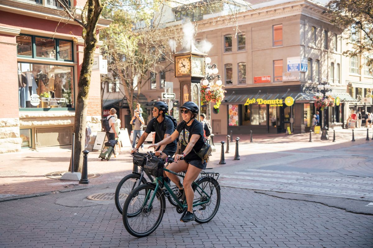 Two cyclists riding down a street in Gastown on a sunny day, as featured in the Grand Bike Tour.