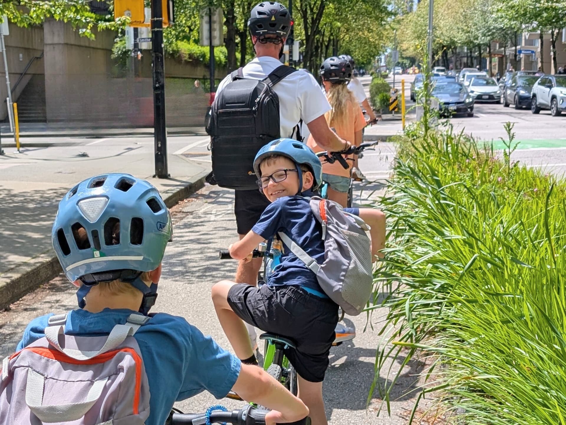 one of the kids in the bike group looks back at the photographer and smiles as they're all stopped along a bike lane.